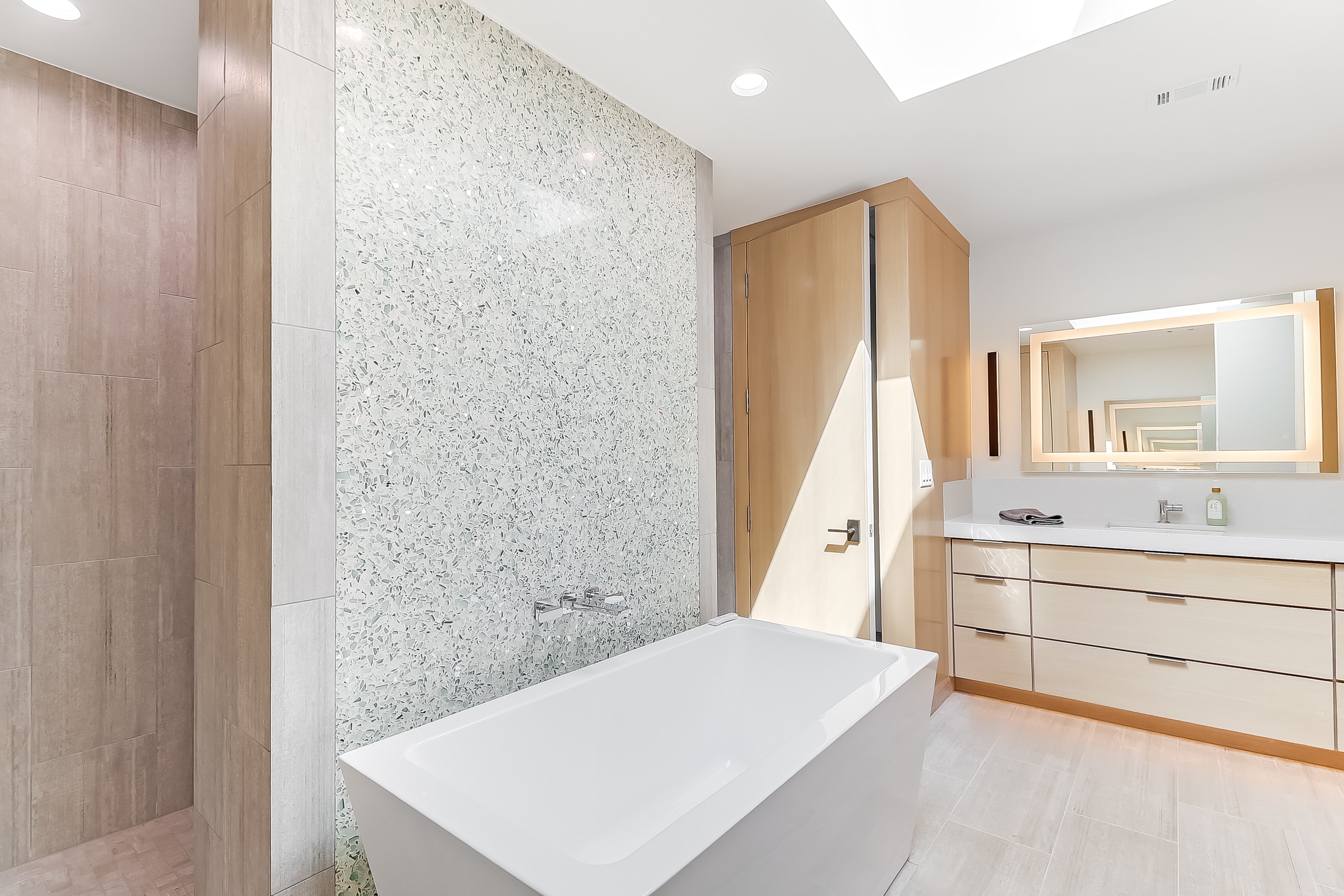 Primary bath with terrazzo accent wall, freestanding tub, and wood cabinetry, The Architect's View